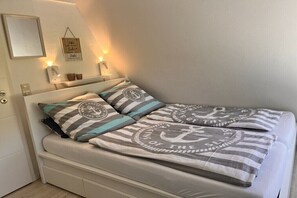 Ein Bett mit gestreifter Bettwäsche und Kissen, ein Nachttisch mit Lampe und eine Wandleuchte.