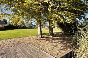 Ein Park mit einer Holzterrasse, einer grünen Rasenfläche und Bäumen mit gelben Blättern.