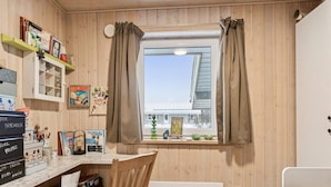 A room with a wooden interior, a window with curtains, a desk with various items, a chair, a radiator, and a bed with a blue mattress. - 4 Star Holiday Home in Hovborg (Hovborg)