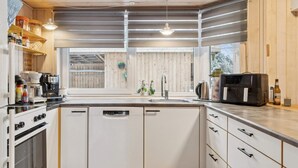 A compact kitchen with white cabinetry, a dishwasher, a stove, and a coffee maker. - 4 Star Holiday Home in Hovborg (Hovborg)