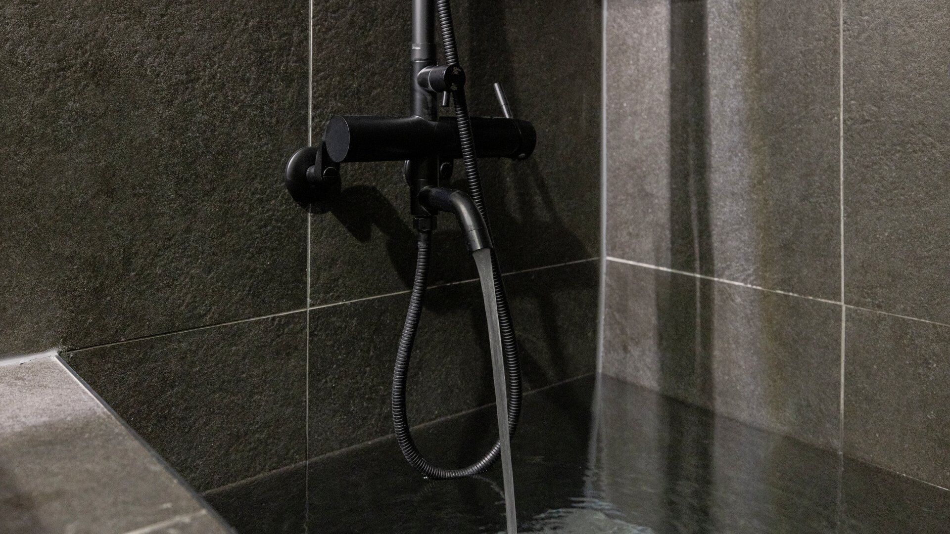 Un cabezal de ducha con manguera flexible en un baño con azulejos.