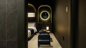 A narrow hallway leading to a bedroom with a bed, a small table with a lamp, and a chair. - Cave Ryokan Hotel by Anook Incheon Bupyeong Station (Incheon)