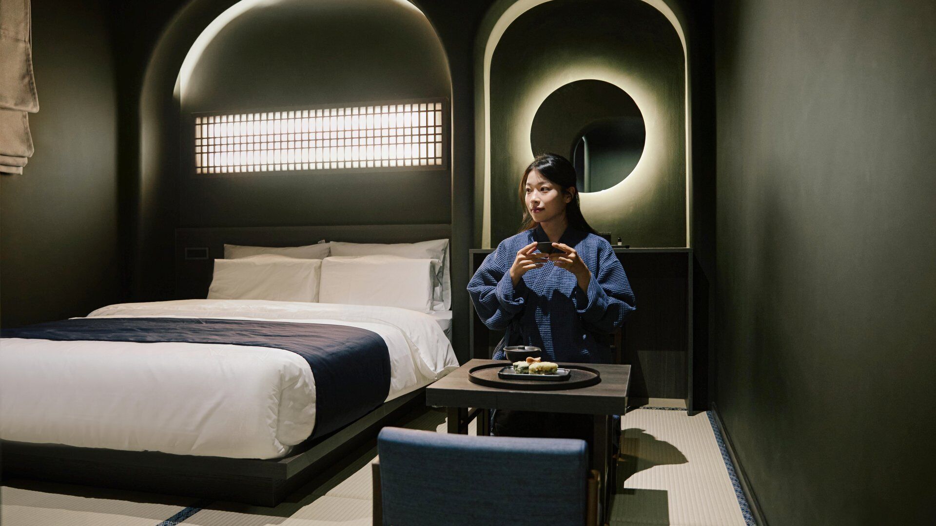 A hotel room with a bed, a table with a bowl of food, and a chair.