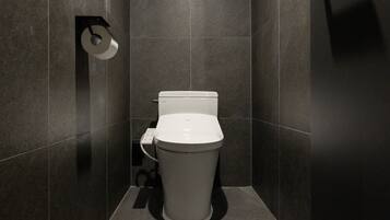 A modern bathroom with a toilet, a toilet paper holder, and a wall-mounted flush handle.