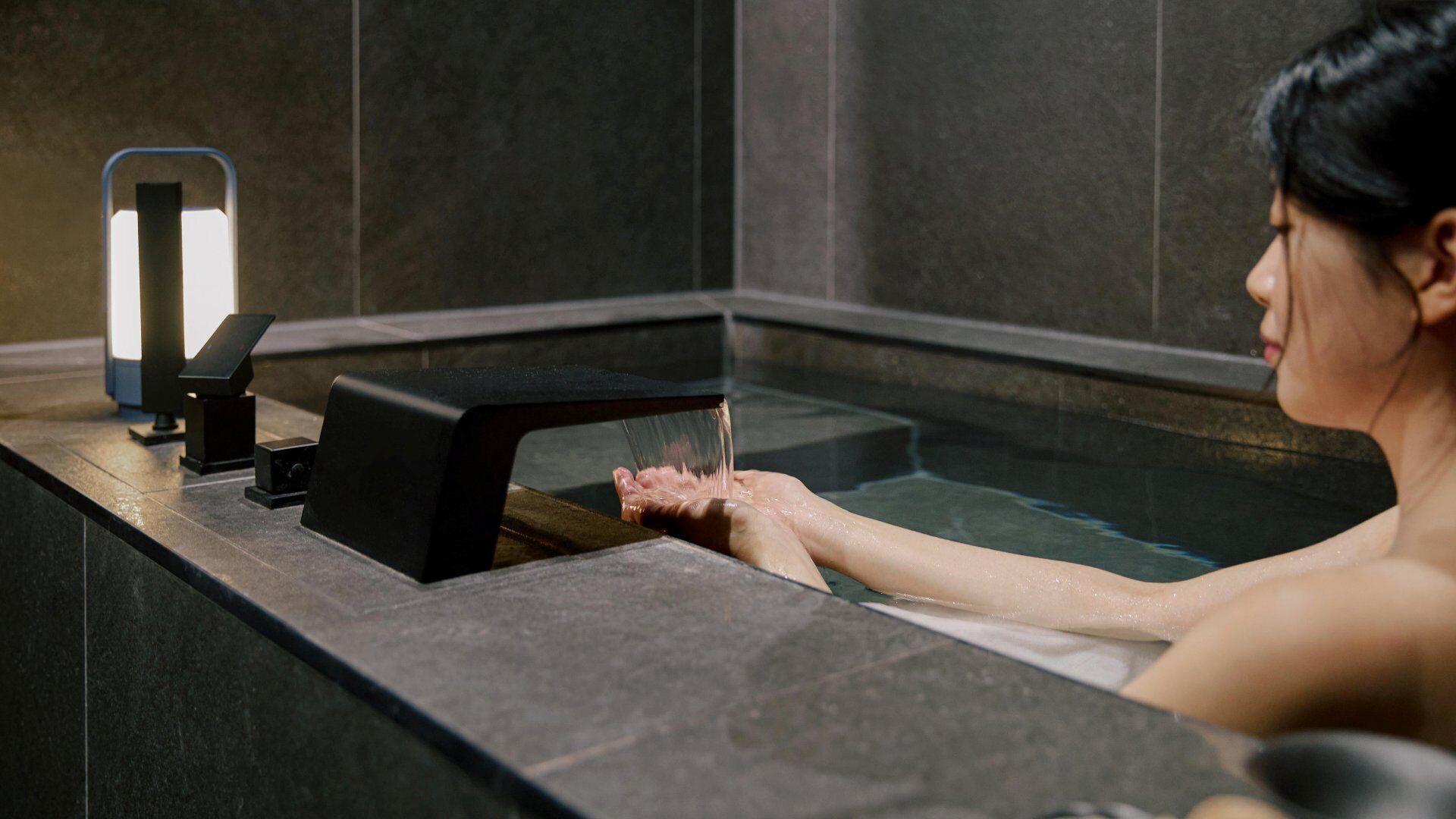 Una persona en una bañera con un cabezal de ducha manual y un panel de control.