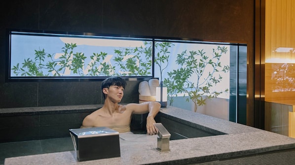 A man in a bathtub with a towel and a box on the counter.