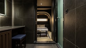 A narrow hallway leading to a bedroom with a bed, bedside table, and bench.