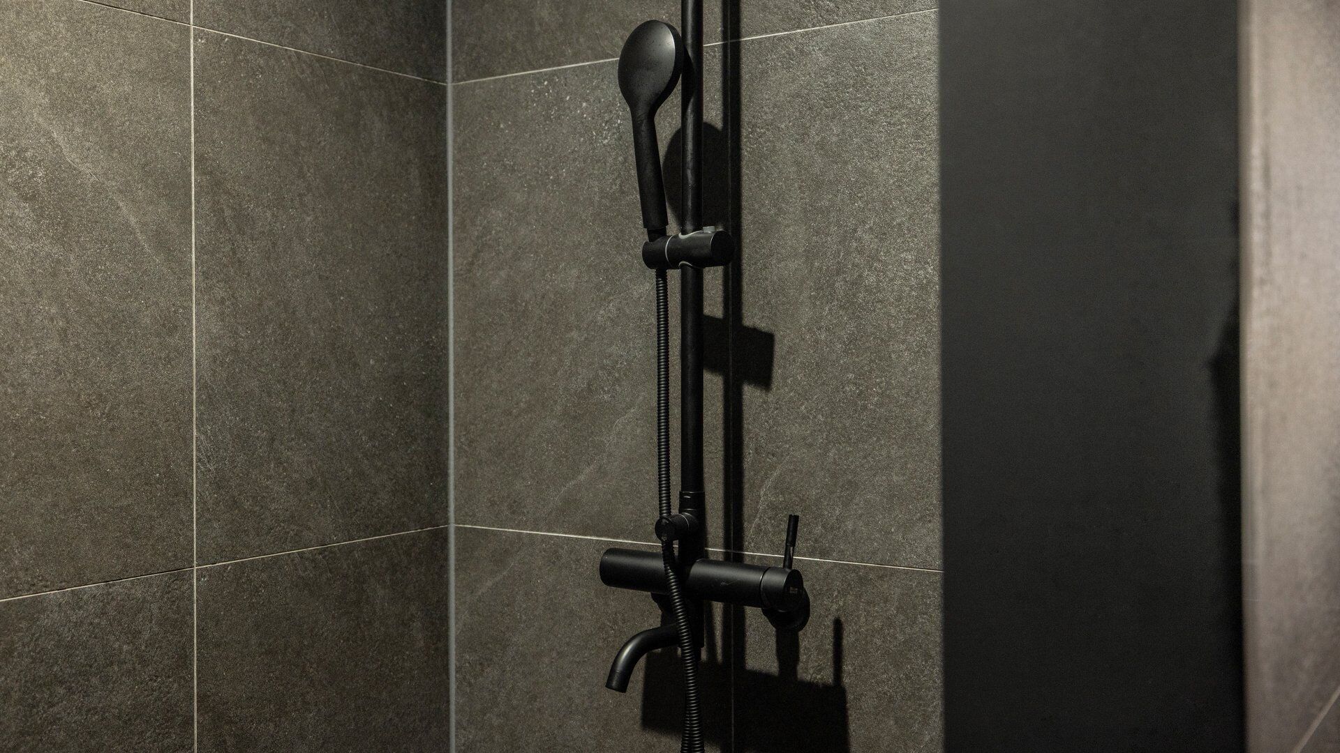 A shower with a handheld showerhead and a fixed wall-mounted faucet.