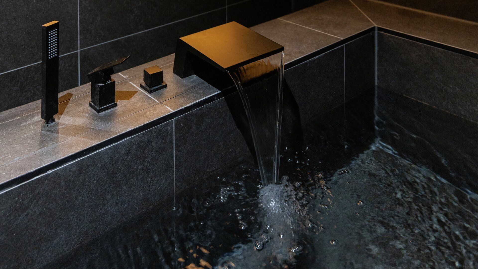 A modern bathroom with a black sink, a handheld showerhead, and a square-shaped mirror.