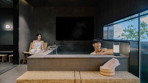 A modern spa with a hot tub, a towel on a bench, and a window with a view of greenery.