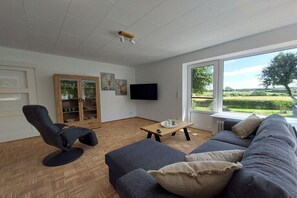 A living room with a sofa, armchair, wooden cabinet, television, and a window with a view of greenery. - Unique landscape view (Stoltebüll)