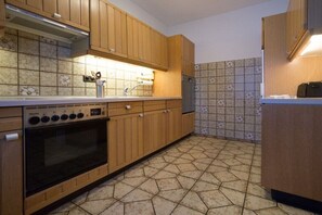 A kitchen with wooden cabinets, a built-in oven, a refrigerator, and patterned floor tiles. - in the Eifelwiese house (Monschau-Höfen)