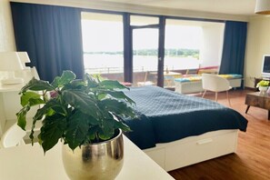 Ein Hotelzimmer mit Bett, Schreibtisch, Stuhl, Zimmerpflanze und Blick auf das Wasser.