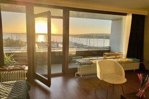 Una habitación con un gran ventanal corredero que da a una vista de un puerto deportivo y al atardecer.