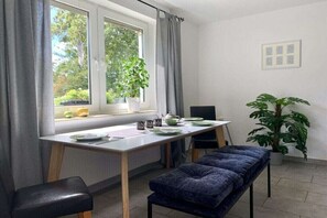 Ein Zimmer mit Esstisch, einer Bank, Topfpflanzen und einem Fenster mit Vorhängen.