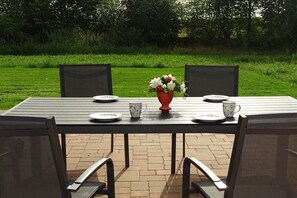 Ein rechteckiger Tisch im Freien mit vier Stühlen, einer Vase mit Blumen und zwei Tassen darauf.