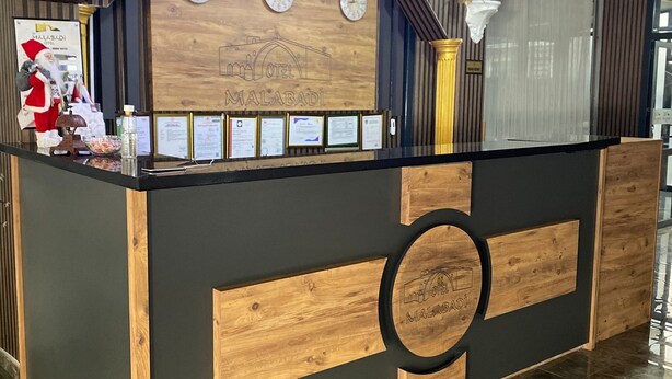 A reception desk with a wooden and black design, featuring a clock, framed certificates, and a Santa Claus decoration. - ÖZ MALABADİ OTEL (Mersin)