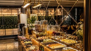 A buffet with various food items and beverages, a wooden counter, and a decorative ceiling structure. - ÖZ MALABADİ OTEL (Mersin)