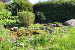 Ein Garten mit Teich, diversen Pflanzen und einem Holzzaun.