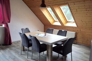 Ein Essbereich mit einem Holztisch und Stühlen, einer Deckenleuchte sowie zwei Oberlichtern.