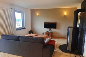 Ein Wohnzimmer mit einer Couch, einem Fernseher, einem Kamin und einem Fenster mit Jalousien.