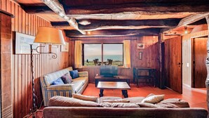 En mysig stuga med träpanel på väggarna, en soffa, ett bord och utsikt över naturen.