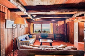 Ein gemütliches Blockhaus-Interieur mit Holzwänden, einer Couch, einem Tisch und Blick ins Freie.