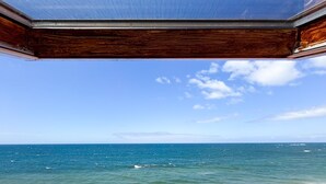 En vy genom ett fönster med träram, med utsikt över en strand, havet och en klar himmel.
