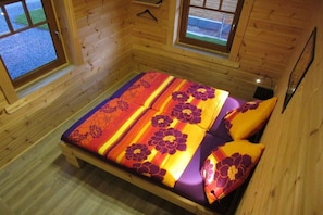 Ein Holzhütten-Zimmer mit einem Bett, zwei Fenstern und Blick ins Freie.