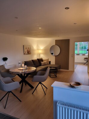 Ein modernes Wohnzimmer mit einer Couch, einem runden Couchtisch und einem Essbereich mit Tisch und Stühlen.