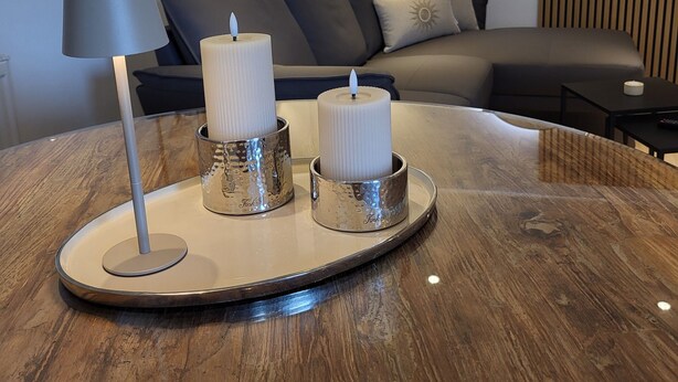 Un salon moderne avec une table basse en bois, deux bougies, une lampe sur pied, un canapé et un miroir fixé au mur.