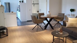 Un salon moderne avec un coin repas, un plancher en bois et une cuisine à l’arrière-plan.
