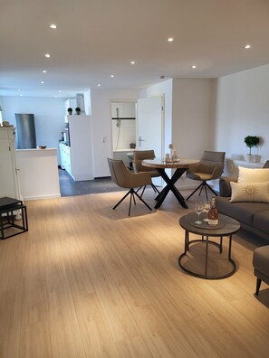 Ein modernes Wohnzimmer mit Essbereich, Holzböden und einer Küche im Hintergrund.