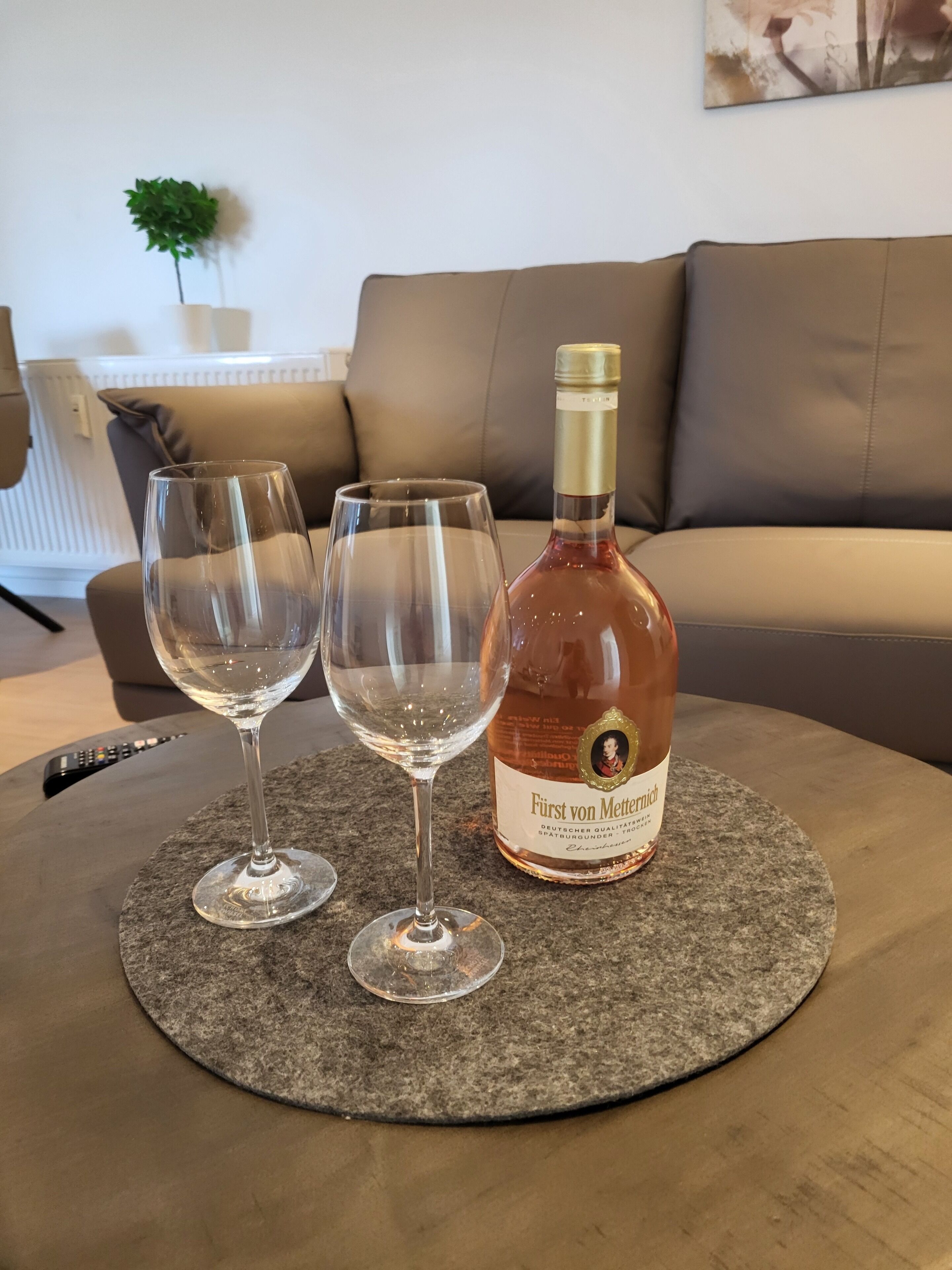 A bottle of wine and two glasses on a round table in a living room.