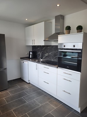 A modern kitchen with white cabinetry, a black marble countertop, a built-in oven, and a dishwasher.