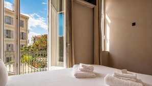 Ein Hotelzimmer mit Bett, weißen Handtüchern, einem Balkon mit Blick auf Gebäude und einem Fenster.