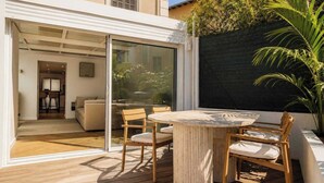 Eine moderne Außenpatio mit einem runden Tisch und Holzstühlen, einer Glastür zu einem Innenraum und einem schwarzen Sichtschutz.