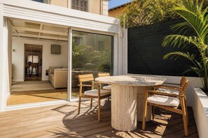 A modern outdoor patio with a round table and wooden chairs, a glass door leading to an interior space, and a black privacy screen. - Duplex Apartment with Pool a/c 2BR/4P - Cannes (Cannes)