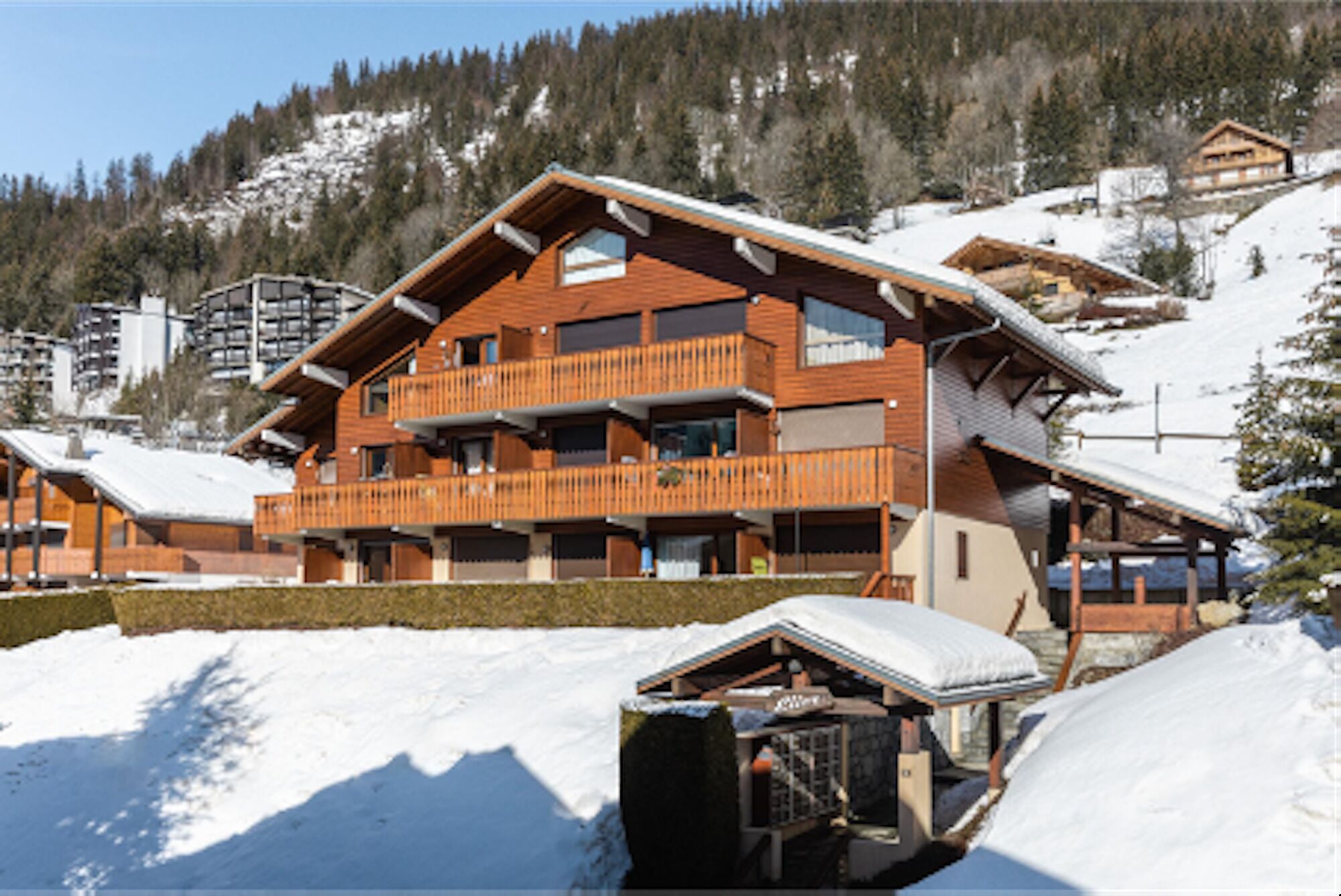 A multi-story wooden building with balconies, surrounded by snow-covered terrain and trees.