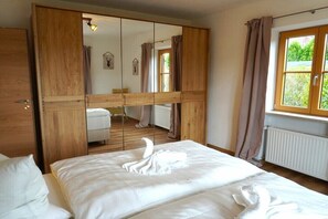 Ein Schlafzimmer mit einem großen Spiegel, einem Holzschrank, einem Bett mit weißen Bettwäsche und einem Fenster mit Vorhängen.