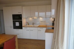Eine kleine Küche mit weißen Schränken, einem schwarzen Backofen und einer Holz Arbeitsplatte.