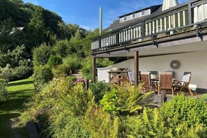 Ein Wohnhaus mit Balkon, Sitzgelegenheit im Freien und üppiger Bepflanzung.