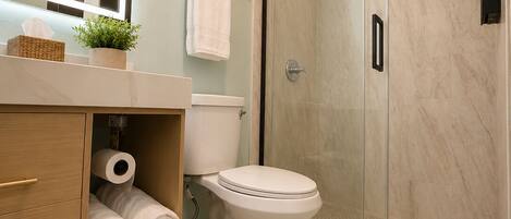 A modern bathroom with a toilet, a shower enclosure, and a vanity with towels.