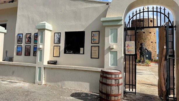 Un edificio con fachada blanca, una reja negra y una estatua al fondo.