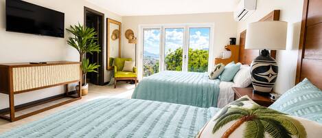 A hotel room with two beds, a TV, a ceiling fan, a plant, and a view of the outdoors.