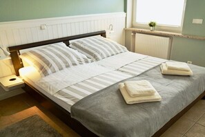 A neatly made bed with striped bedding and folded towels, a bedside table with a lamp, and a window with a view of the outside. - Holiday apartment with 2 bedrooms (Cuxhaven)