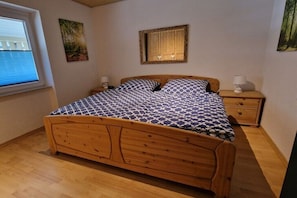 Ein hölzernes Bett mit einem gemusterten Bettbezug, ein Nachttisch mit Lampe und ein Fenster mit Jalousien.