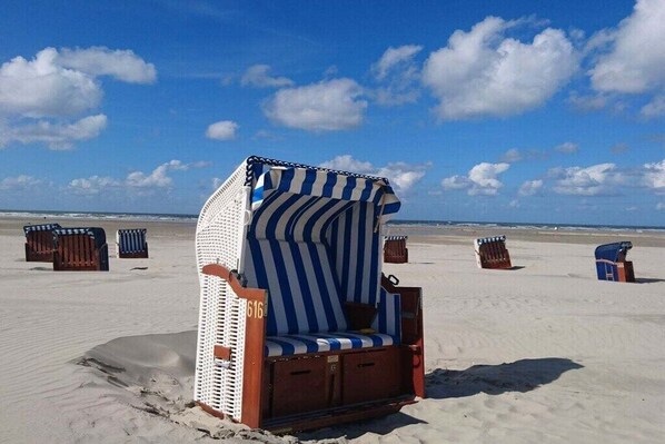 Ein Liegestuhl mit Streifenmuster, der mit der Nummer '616' beschriftet ist, vor einer Strandkulisse mit Sand und blauem Himmel.