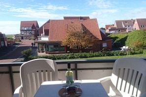 Ein Balkon mit zwei weißen Stühlen, einer Weinflasche und zwei Weingläsern auf einem Tisch.