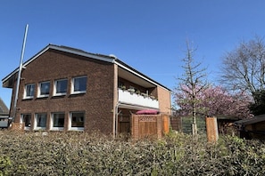 Ein zweistöckiges Ziegelhaus mit Balkon, Holzzaun und einem Baum mit rosa Blüten.
